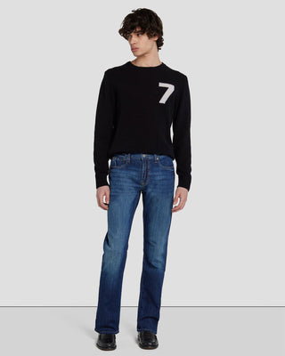 A male model wearing a black sweater with the number 7 on it and a pair of blue straight-leg jeans.