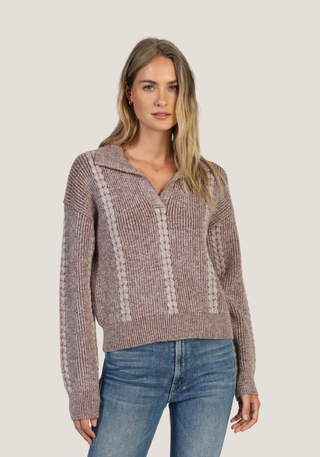 A woman modeling a ribbed knit sweater with a collar and vertical textured stripe details, paired with blue jeans, against a solid light gray background.