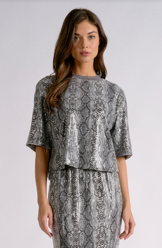 A woman modeling a matching two-piece outfit featuring a metallic snakeskin print. The set includes a short-sleeve top with a crew neck and a matching high-waisted skirt.