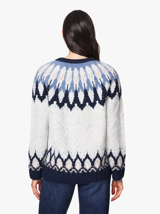 A woman viewed from the back wearing a knitted sweater with a Fair Isle pattern in cream, light blue, and navy, paired with blue jeans against a plain white background.