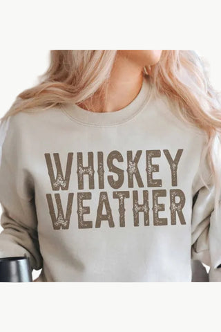 Beige sweatshirt with 'WHISKEY WEATHER' text worn by a person with blonde hair.