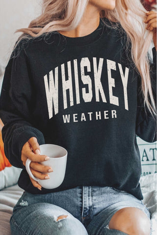 Person wearing a black sweatshirt with 'WHISKEY WEATHER' text, holding a white mug.