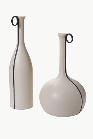 Two ceramic vases, one tall with a narrow neck and a small circular handle at the top, the other is round and broader at the top with a similar handle. Both have a matte white finish with black stripes.