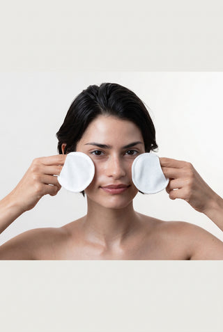 Woman holding white cotton pads in front of her eyes against a plain background