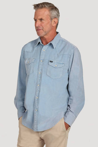 A man wearing a light blue long-sleeve western-style button-up shirt with two chest pockets, paired with khaki pants, photographed against a plain light gray studio background.