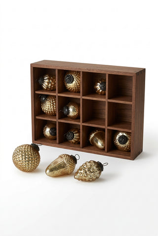A set of gold-colored glass Christmas ornaments with antique golden acorn, pinecone, and glass orb designs displayed in a brown box.